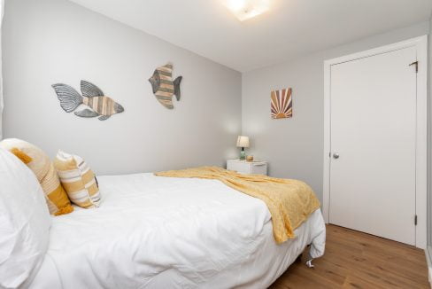 A neatly made bed with white linens in a modern bedroom with wooden flooring and fish-themed wall art.