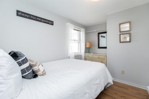 A neatly arranged bedroom with a white bedspread, a decorative wall sign reading 