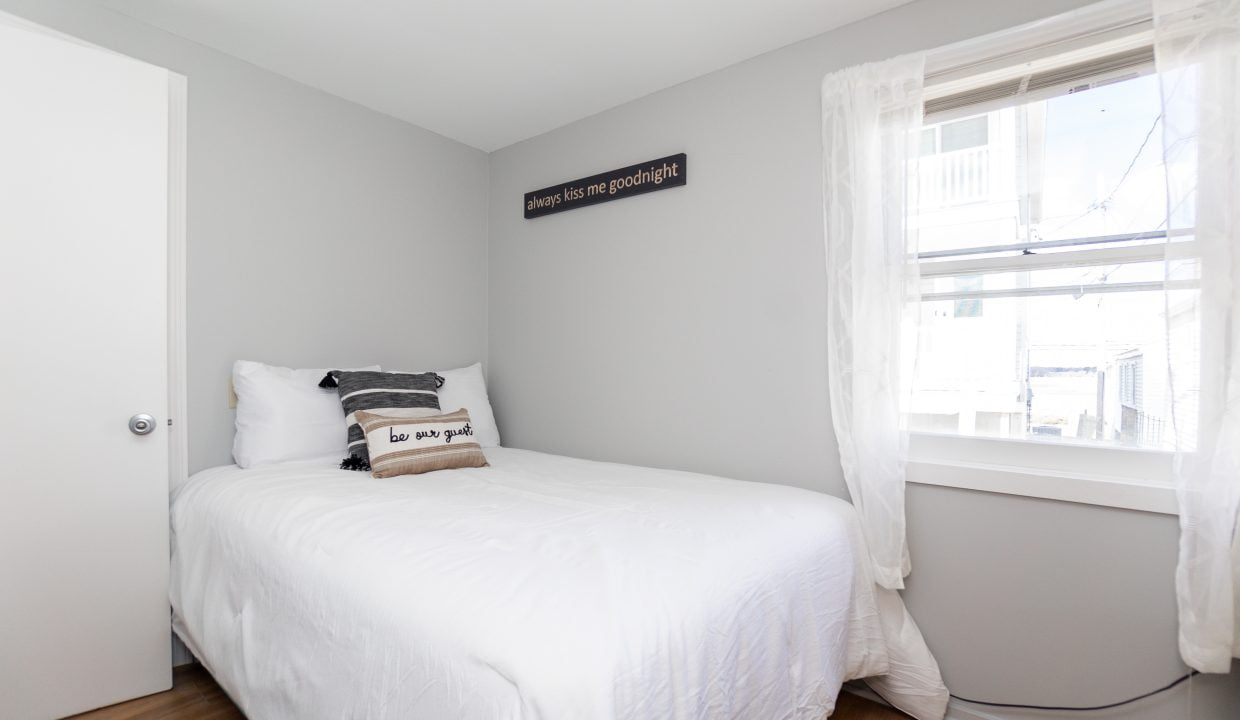 Minimalist bedroom with a single white bed, a decorative pillow, and a wall sign that reads 