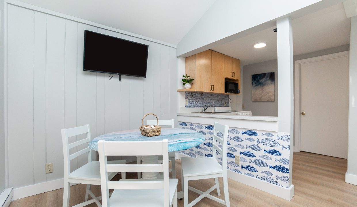 Modern compact kitchenette with a white dining area and wall-mounted television.
