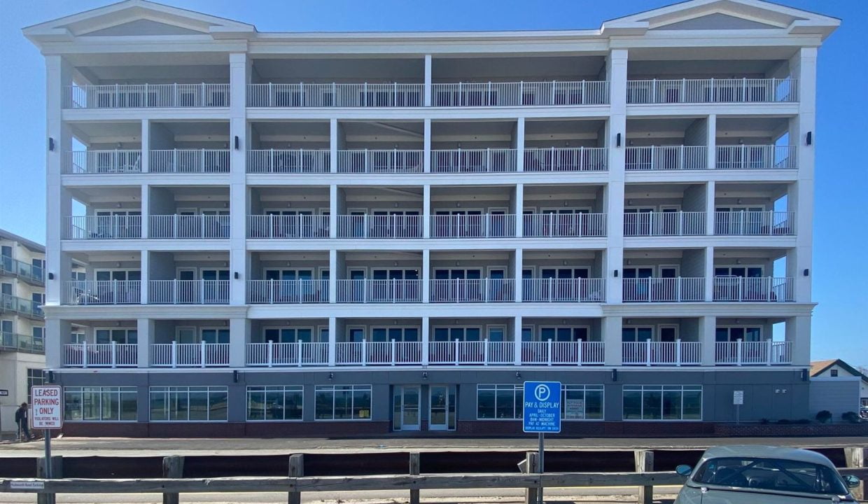 A modern multi-story apartment building with balconies, under a clear blue sky.