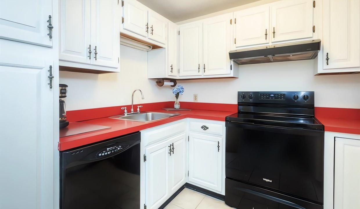 Modern kitchen interior with white cabinets, red countertops, and black appliances, including a stove and oven.