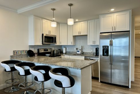 Modern kitchen interior with bar stools, stainless steel appliances, and white cabinetry.