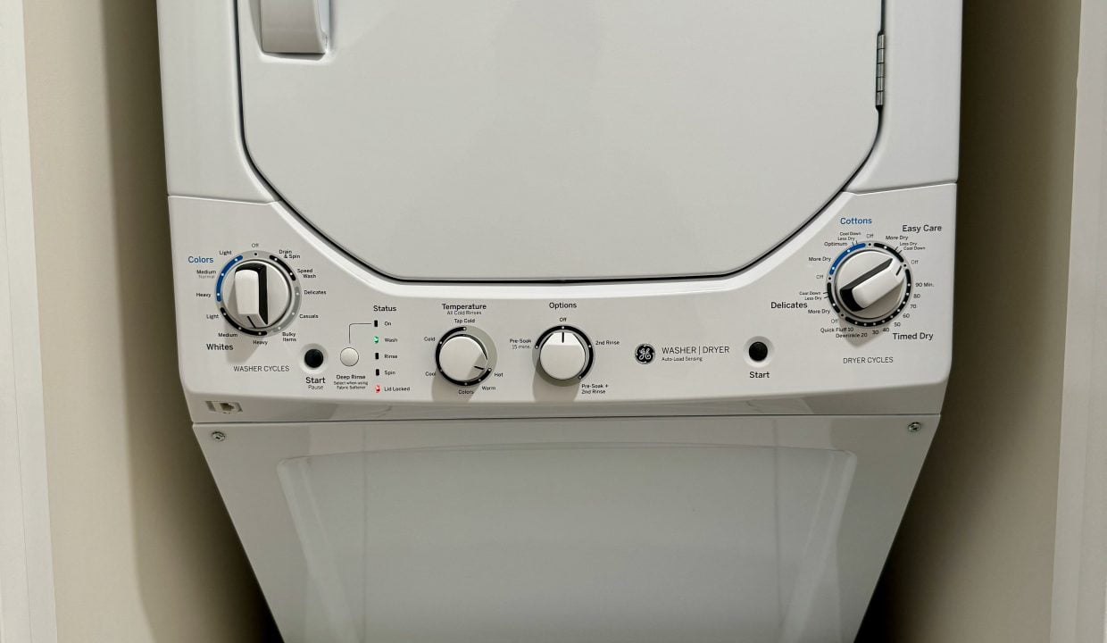 Stacked white washing machine and dryer in a laundry room.