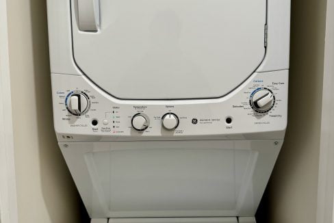 Stacked white washing machine and dryer in a laundry room.