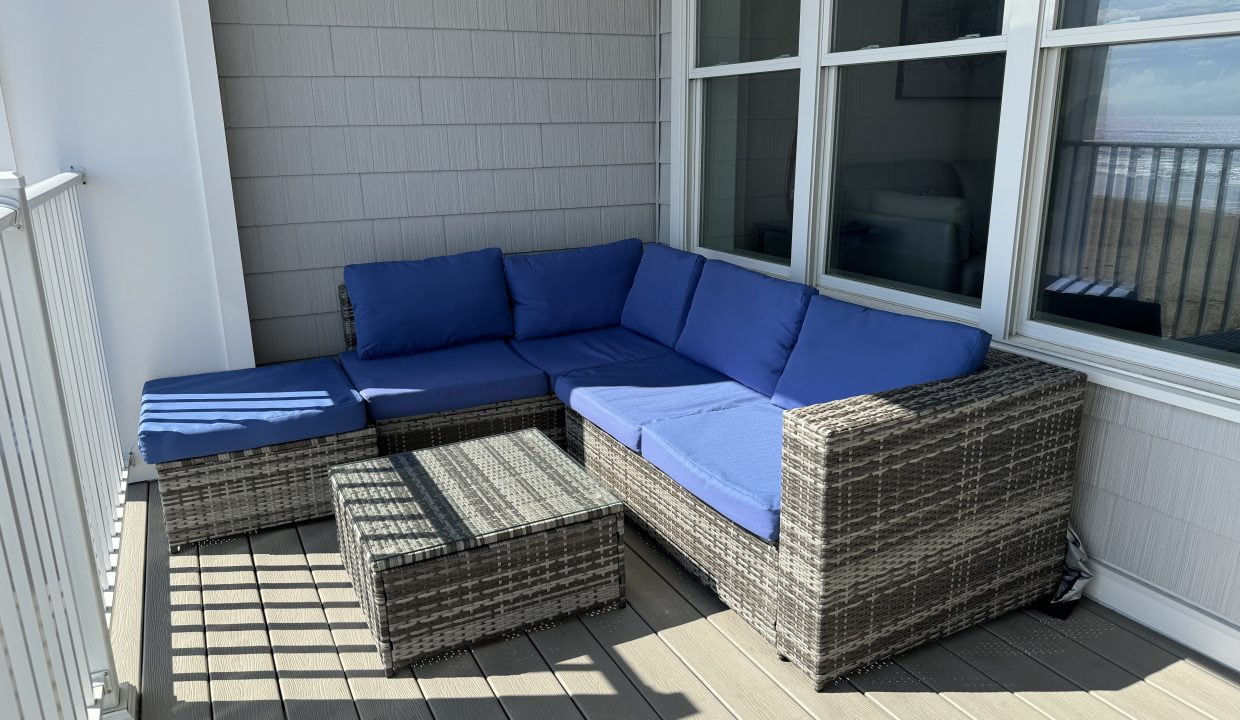 Outdoor patio furniture with blue cushions on a sunny balcony overlooking the water.