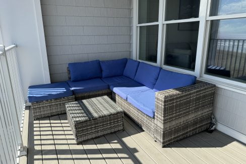 Outdoor patio furniture with blue cushions on a sunny balcony overlooking the water.