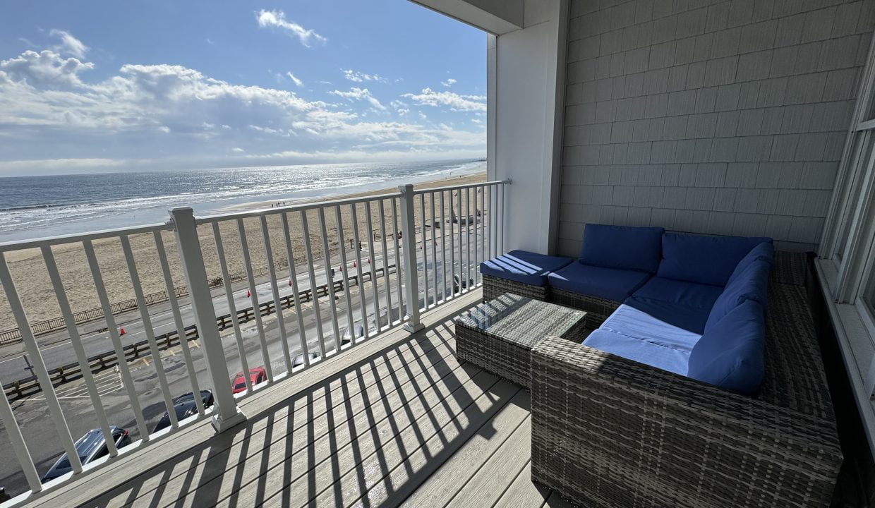 Oceanfront balcony with outdoor furniture overlooking the beach on a sunny day.