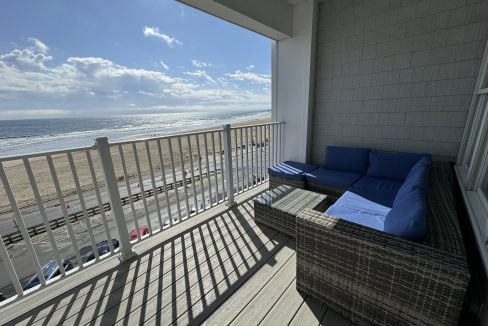 Oceanfront balcony with outdoor furniture overlooking the beach on a sunny day.