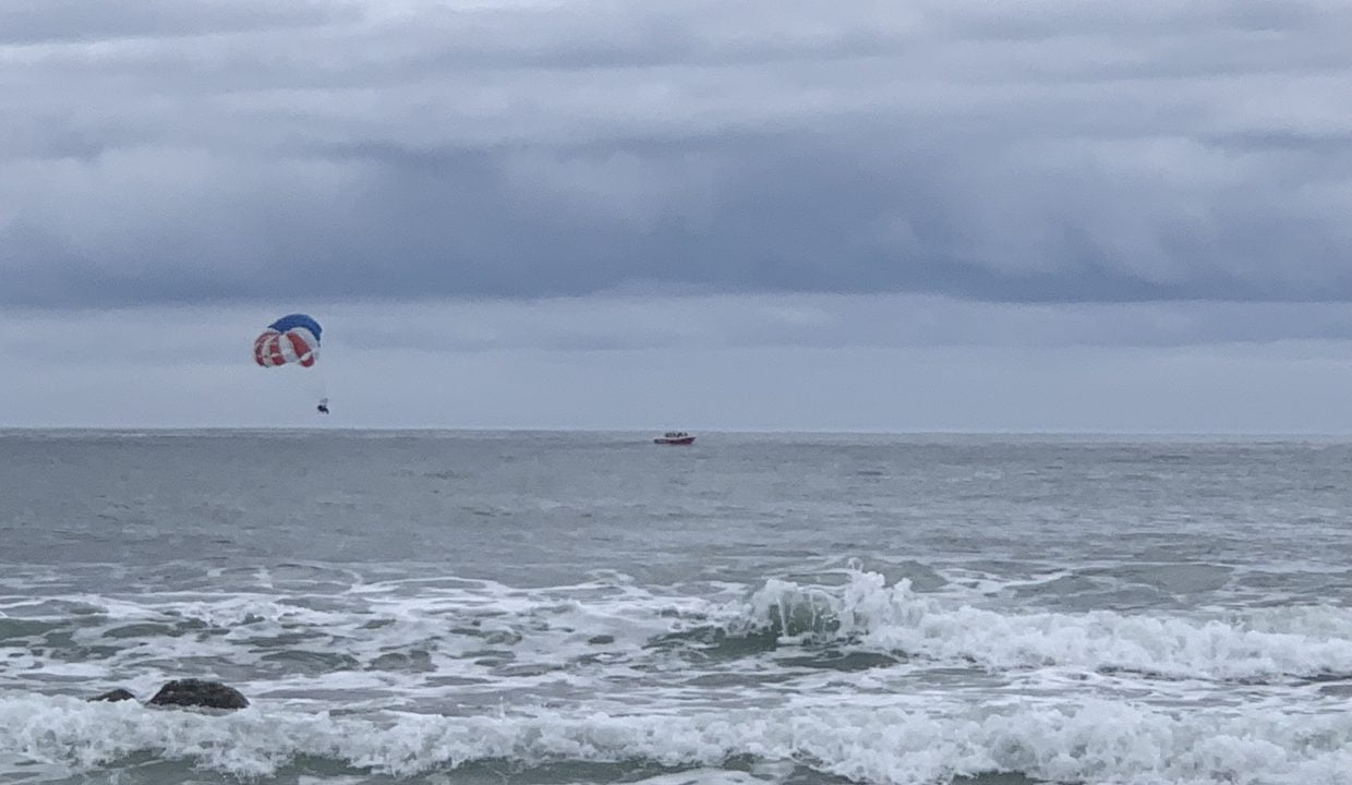 A parasailer above choppy sea waters under overcast skies.