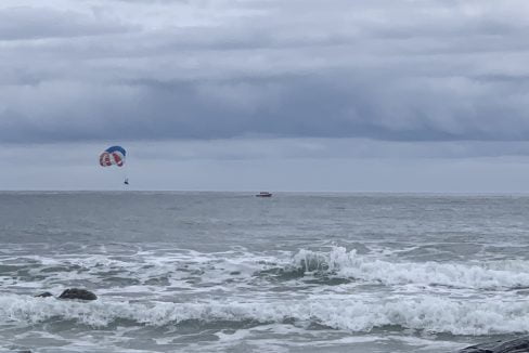 A parasailer above choppy sea waters under overcast skies.