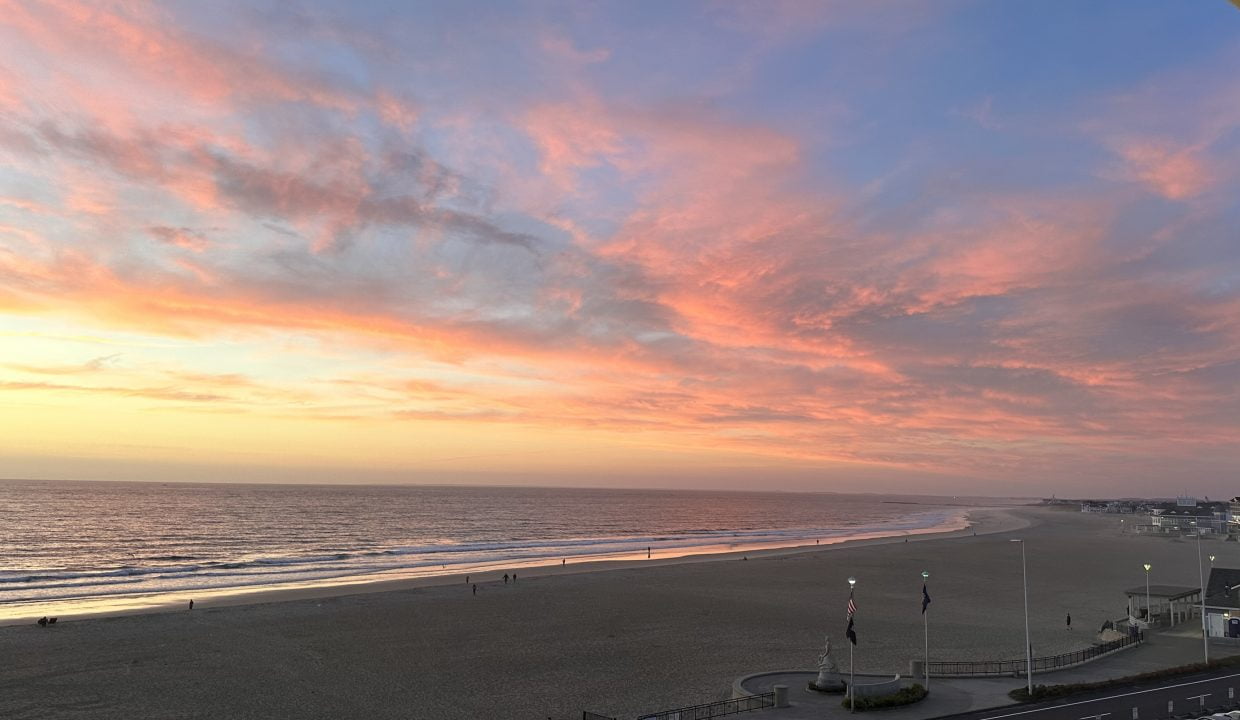 A coastal sunset with vivid pink and orange clouds over a tranquil beach and calm sea.