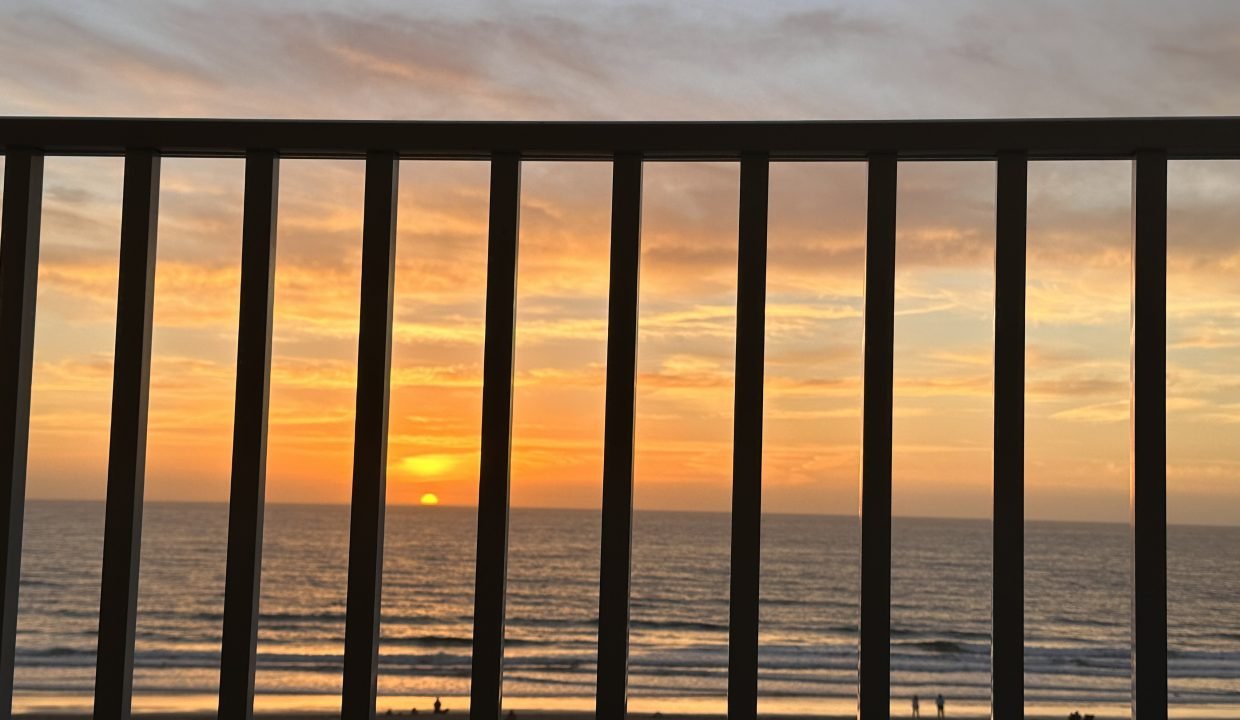 Sunset viewed through balcony railings overlooking the beach.