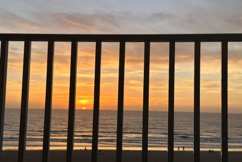 Sunset viewed through balcony railings overlooking the beach.