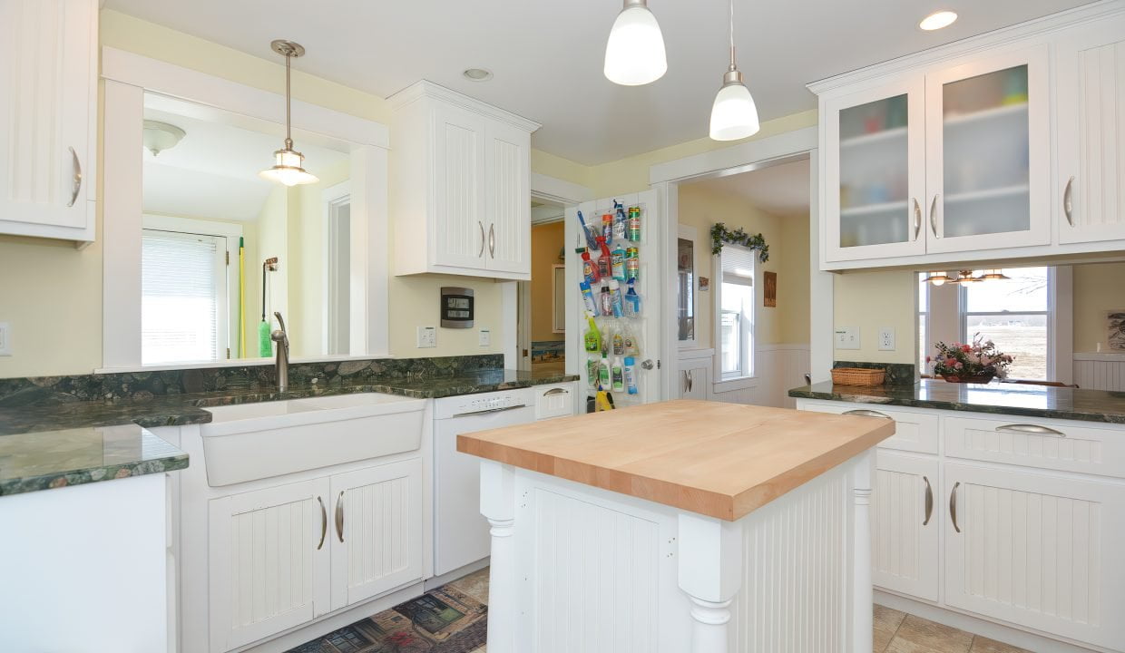 Bright, spacious kitchen with white cabinetry, granite countertops, and a central wooden island, illuminated by pendant lights.