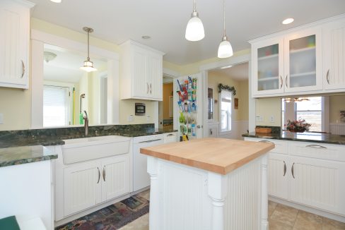 Bright, spacious kitchen with white cabinetry, granite countertops, and a central wooden island, illuminated by pendant lights.