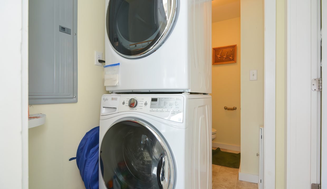 A stackable washer and dryer in a small, tidy laundry room with an open door leading to a bathroom.