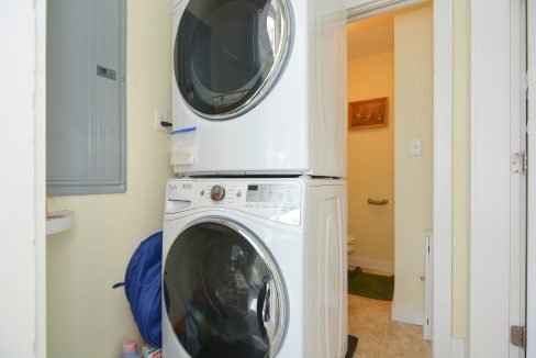 A stackable washer and dryer in a small, tidy laundry room with an open door leading to a bathroom.
