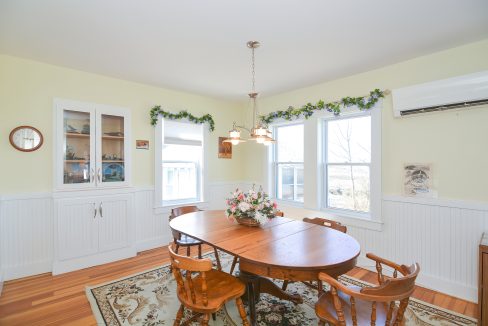Bright dining room with oval wooden table, chairs, wall sconces, and large windows. decor includes a floral centerpiece and hanging greenery.