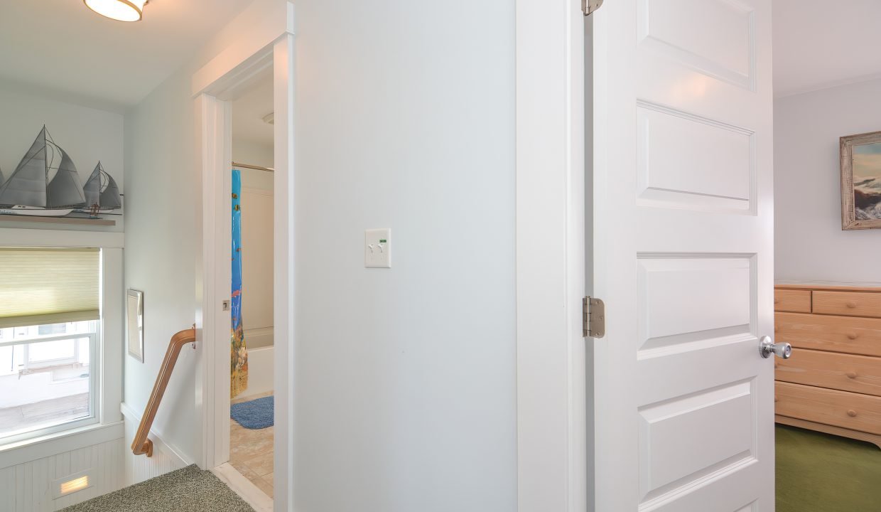 A bright hallway with an open door leading to a staircase, a closed wooden door on the right, and nautical-themed decorations.