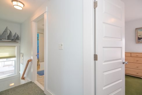A bright hallway with an open door leading to a staircase, a closed wooden door on the right, and nautical-themed decorations.