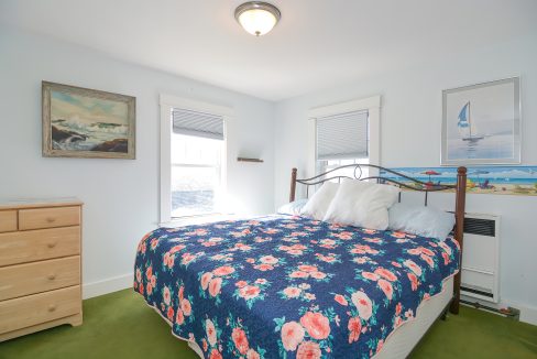 A bright, neatly arranged bedroom with a floral bedspread, wooden furniture, and framed artwork on the walls.