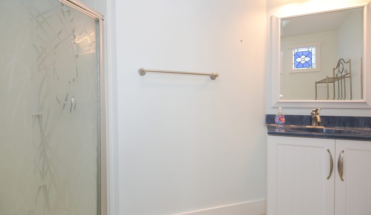 A modern bathroom featuring a glass shower enclosure, a white vanity with blue countertop, and a mirror with a decorative window design.