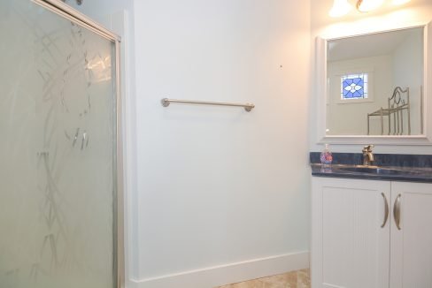 A modern bathroom featuring a glass shower enclosure, a white vanity with blue countertop, and a mirror with a decorative window design.