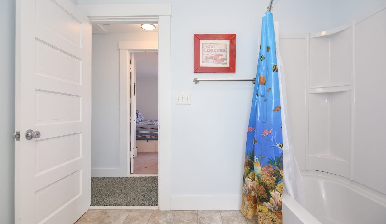 A small, well-lit bathroom featuring a bathtub with a colorful marine life shower curtain, a white door opened to a hallway, and marine-themed decor.