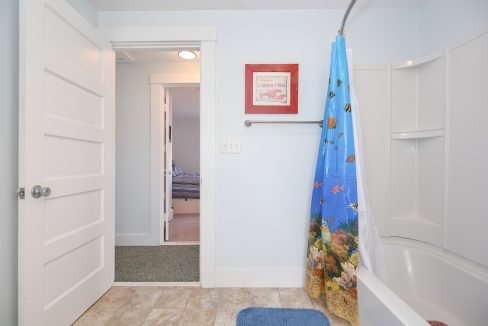 A small, well-lit bathroom featuring a bathtub with a colorful marine life shower curtain, a white door opened to a hallway, and marine-themed decor.