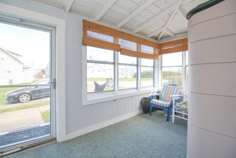 Bright, enclosed porch with wide windows, blue cushioned chairs, and bamboo blinds, overlooking a quiet residential street.