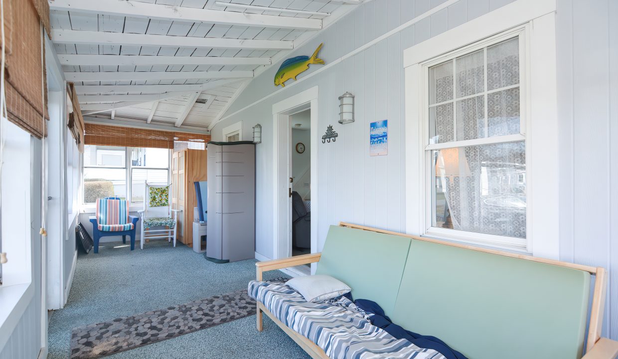 Bright, coastal-style sunroom with white walls, a blue sofa, fish decor, and large windows overlooking a sunny porch.