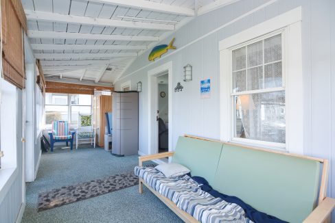 Bright, coastal-style sunroom with white walls, a blue sofa, fish decor, and large windows overlooking a sunny porch.