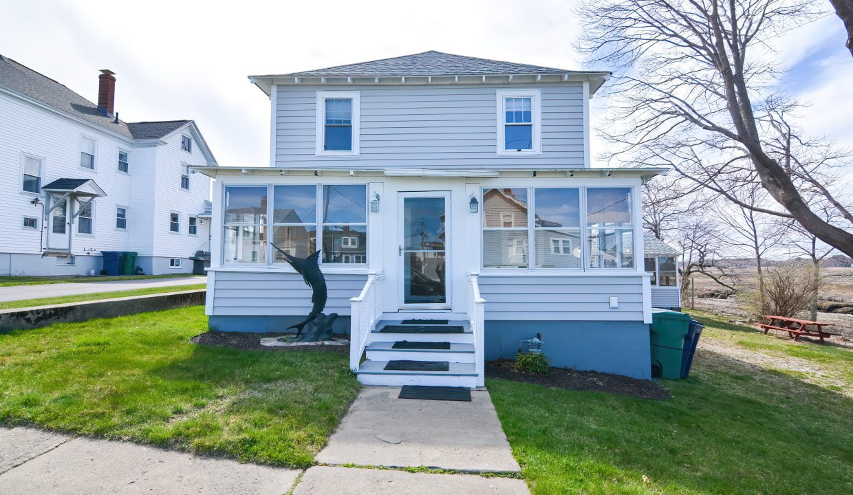 A two-story blue and white house with a screened porch, front steps, and bare trees nearby under a clear sky.