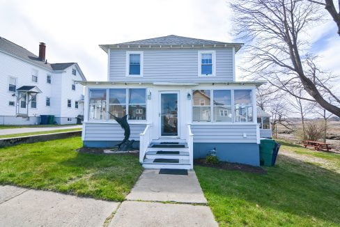 A two-story blue and white house with a screened porch, front steps, and bare trees nearby under a clear sky.