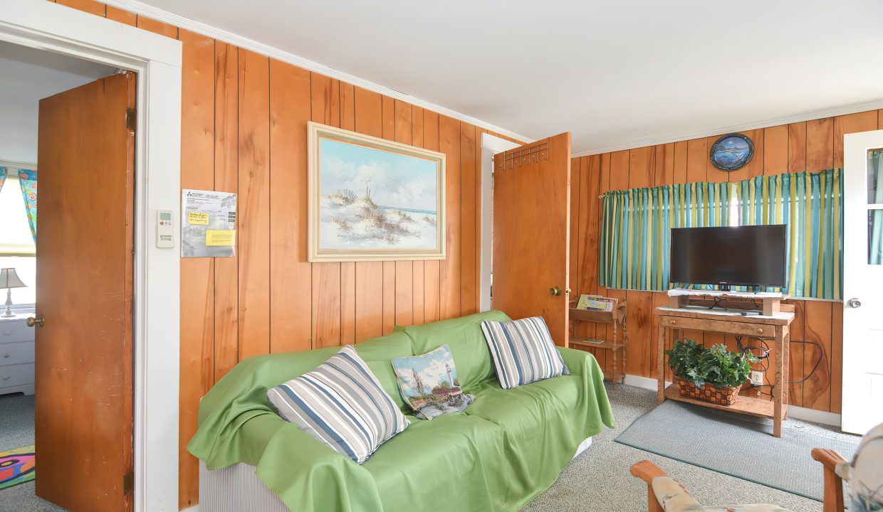 Cozy living room with wooden paneling, a green sofa, striped pillows, a tv, and maritime-themed decor.