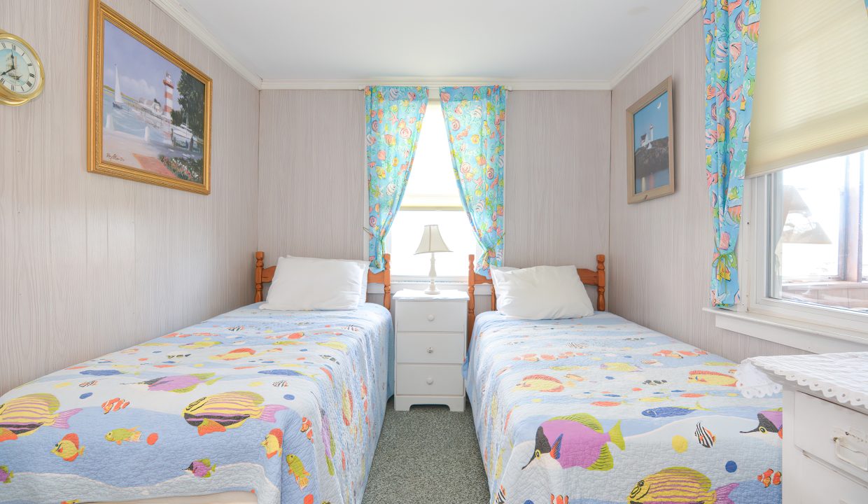 A bright, tidy bedroom with two single beds covered in colorful fish-patterned bedding, pink walls, and a seaside-themed decor.