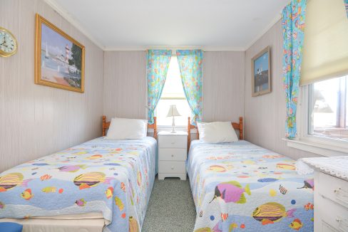 A bright, tidy bedroom with two single beds covered in colorful fish-patterned bedding, pink walls, and a seaside-themed decor.