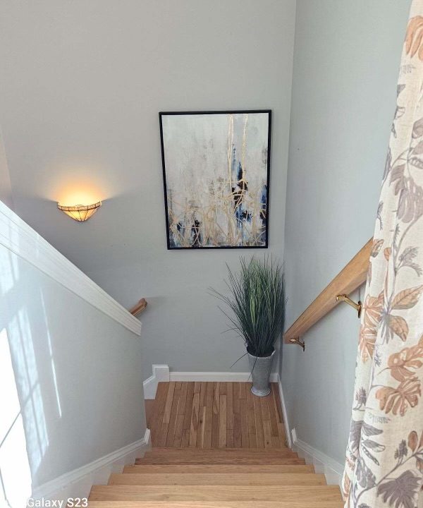 A stairway landing with an abstract painting on the wall, a wall sconce, and a decorative plant beside the wooden stairs.