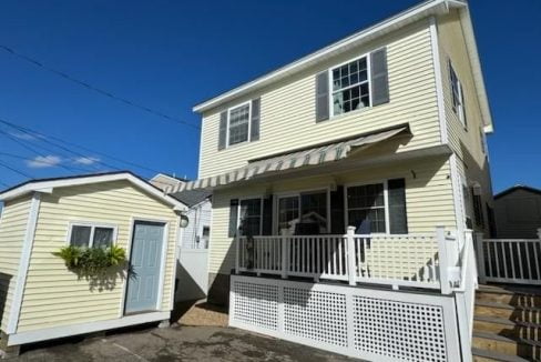 Two-story beige house with white trim and a small attached structure under a clear blue sky.