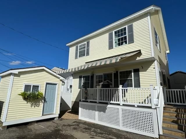 Two-story beige house with white trim and a small attached structure under a clear blue sky.