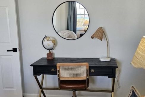 A cozy workspace with a black desk, a mid-century style chair, and a circular mirror on the wall.