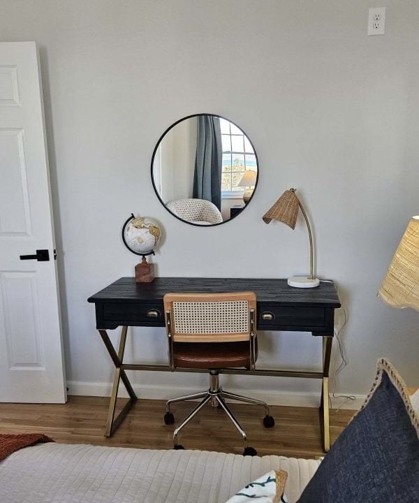 A cozy workspace with a black desk, a mid-century style chair, and a circular mirror on the wall.