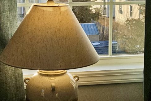 Table lamp on a windowsill with a view of a coastal landscape during sunset.
