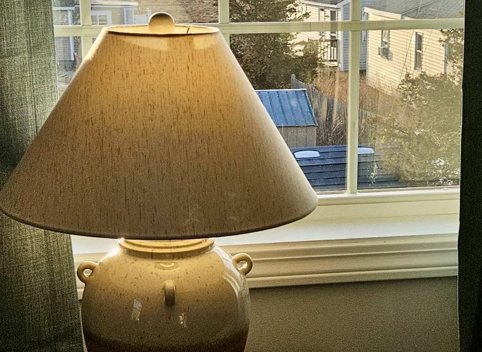 Table lamp on a windowsill with a view of a coastal landscape during sunset.