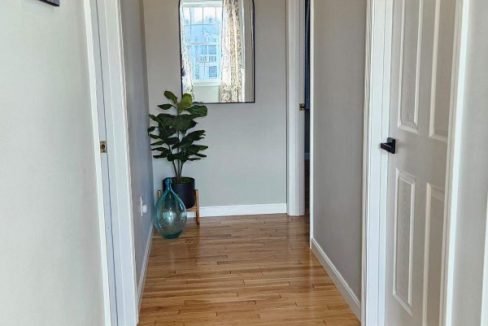 A bright hallway featuring wooden floors, white doors, and a decorative mirror on the wall.