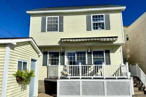 Two-story pale yellow house with white trim and a front porch under a clear blue sky.