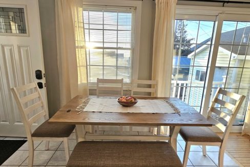 A bright dining room with a wooden table set, light curtains, and a view of a patio area through sliding doors.