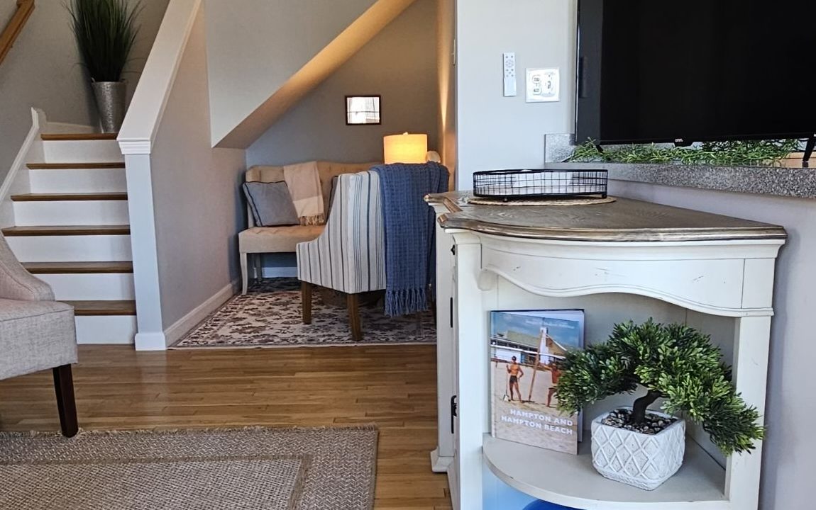 A cozy living room corner with a staircase, a lamp on a side table, and a television set, featuring decorative elements and a neutral color palette.