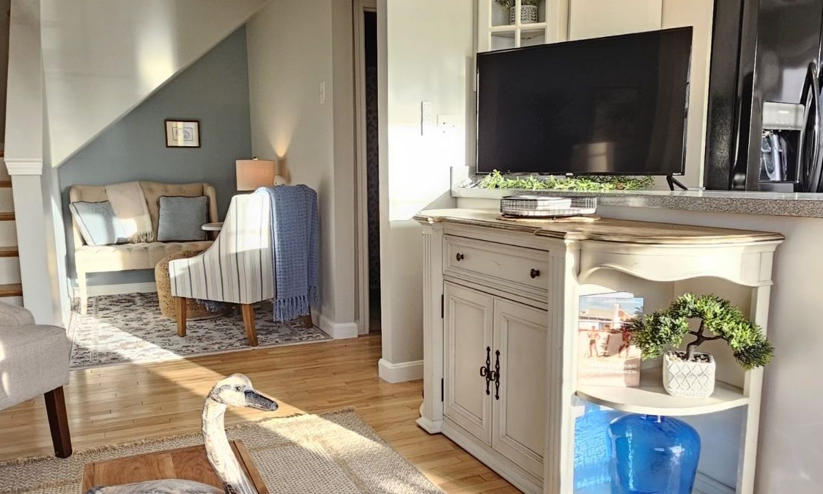 Bright living area with a sectional sofa, white cabinetry, and decorative elements, leading into a cozy nook.